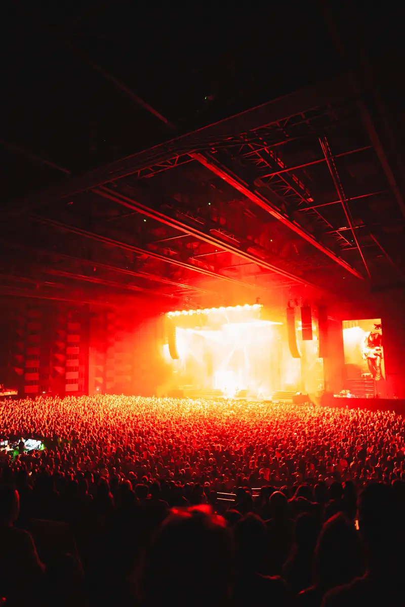 Concert en grande salle, scène rouge et public en silhouette