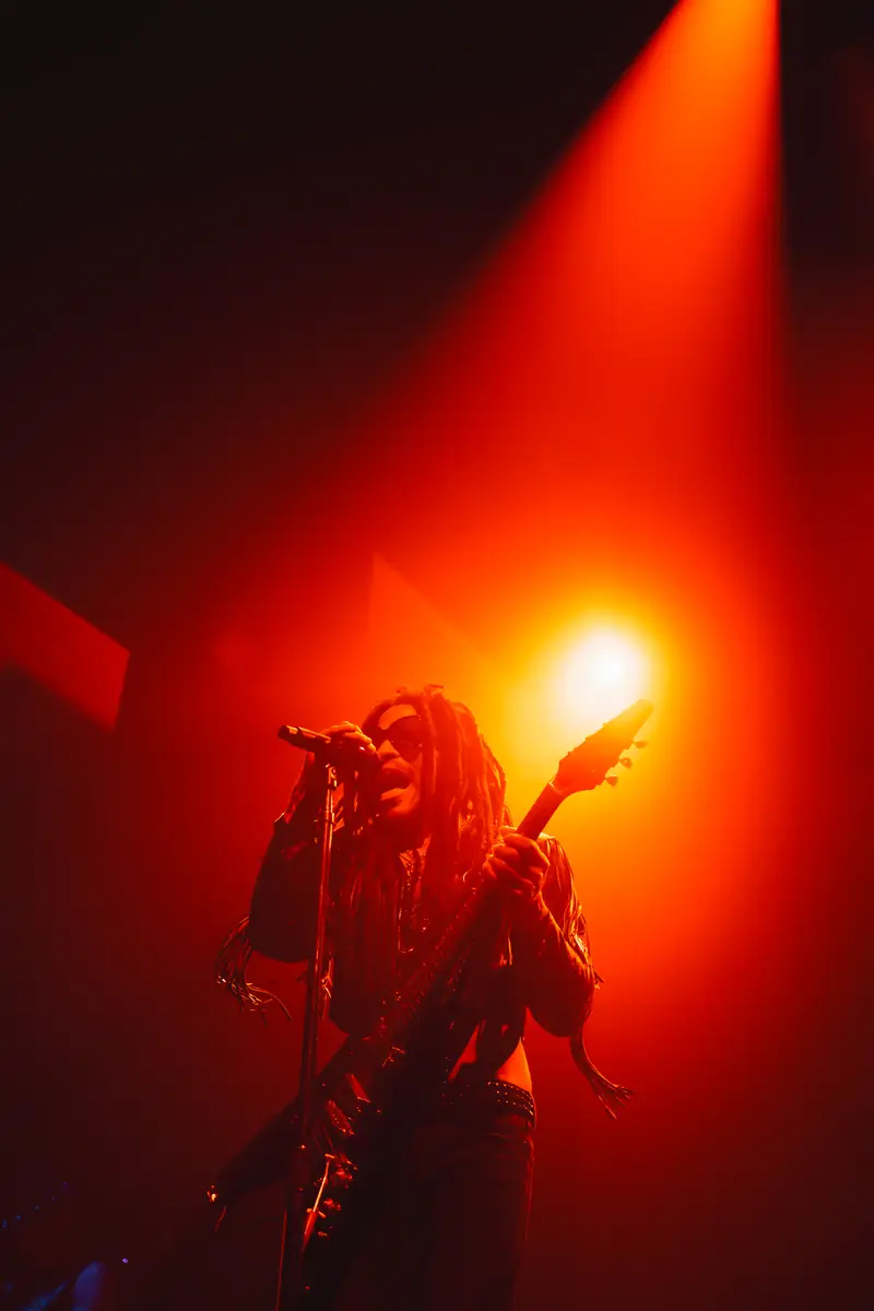 Lenny Kravitz au micro et à la guitare dans une lumière rouge