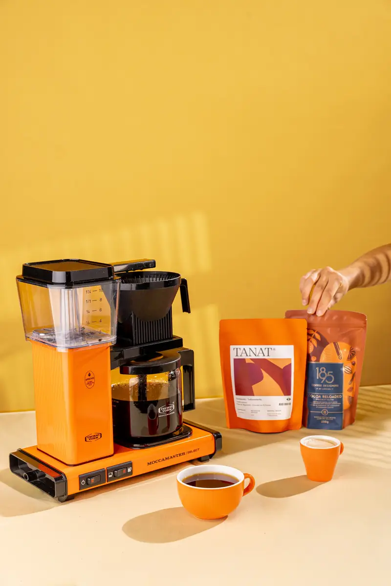 Cafetière filtre orange, tasses et paquet de café sur fond jaune