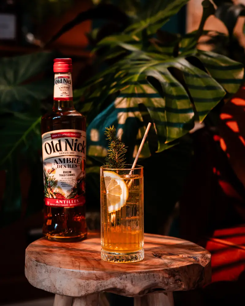 Old Nick ambré et cocktail sur un tabouret en bois, plantes tropicales